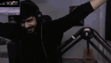 a man wearing headphones stands in front of a microphone with his arms outstretched and a guitar in the background