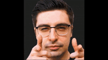 a man wearing glasses is pointing at the camera with both hands