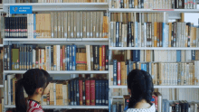 two girls are looking at books in a library with a sign that says upfront works