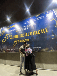 a couple kissing in front of a sign for the 50th commencement exercises