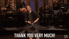 a man in a kilt says thank you very much in front of an orchestra