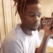 a man with dreadlocks is sitting in a chair holding a cell phone .