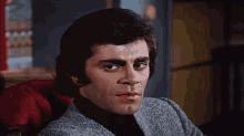 a man wearing a turtleneck and a gray jacket looks at the camera