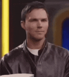 a man in a leather jacket is looking at something while sitting in front of a yellow light .