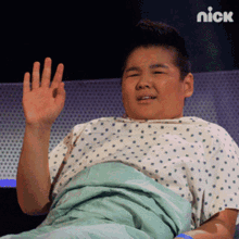 a boy in a hospital gown is waving his hand in front of a nick logo