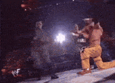 a wrestler in yellow pants is kneeling down in front of a crowd with a wwe logo in the background