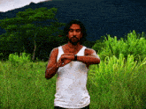 a man in a white tank top is standing in a grassy field