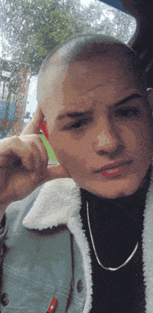 a man with a shaved head is wearing a black turtleneck and a denim jacket