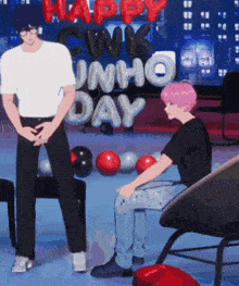 a man standing next to another man in front of a sign that says happy gwk unho day