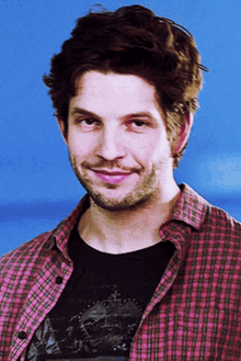 a man wearing a plaid shirt and a black t-shirt smiles for the camera
