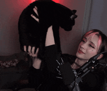 a girl with pink hair holds a black cat in her arms