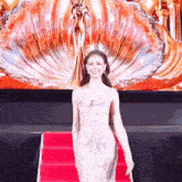 a woman in a white dress is walking down a red carpet in front of a large screen .