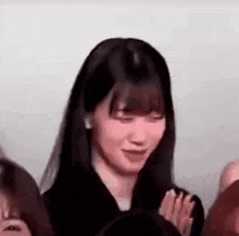 a woman with long black hair is standing in front of a group of people and smiling .