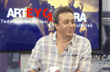 a man in a plaid shirt is smiling in front of a screen that says arteygra