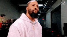 a man with a beard and a pink hoodie is standing in a room .