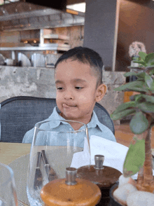 a young boy sits at a table with a glass and a pepper mill