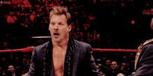 a man in a suit is standing in a wrestling ring with his mouth open and a surprised look on his face .
