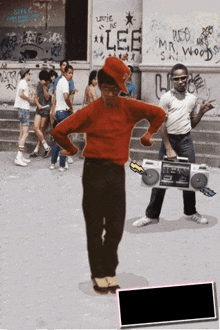 a man in a red shirt is holding a boombox in front of a building that has lee written on it