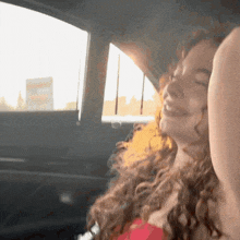 a woman with curly hair is sitting in the back seat of a car with her eyes closed