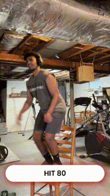 a man in a grey shirt is jumping over a chair that says hit 80 on the bottom
