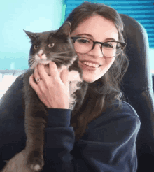 a woman wearing glasses holds a cat in her lap