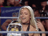 a woman in a wrestling ring holding a championship belt and smiling .
