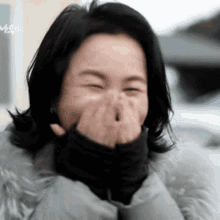 a woman in a fur coat is laughing with her hands over her mouth