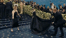 a woman in a black dress is being helped up the stairs by people .