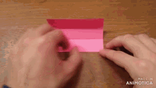 a person is holding a piece of pink paper on a table .