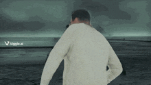 a man in a white sweater is standing in front of a body of water with a viggle.ai logo on the bottom right
