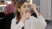 a woman is applying mascara on her eyebrows