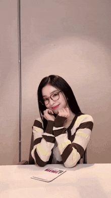 a girl wearing glasses and a striped sweater is sitting at a table .