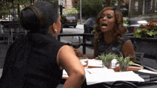 two women are sitting at a table drinking wine and having a conversation .