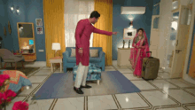 a man in a red kurta points at a woman in a pink dress in a living room