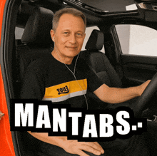 a man wearing headphones is sitting in the driver 's seat of a car with the word mantabs on the bottom right