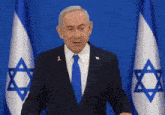 a man in a suit and tie stands in front of two flags with a star of david on them