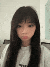 a girl with long hair is wearing a white t-shirt with the letter t on it