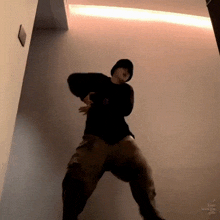 a man in a black hoodie and khaki pants is standing in front of a wall .