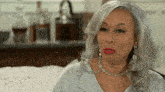 a woman with gray hair and red lips is sitting on a couch