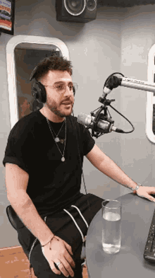 a man wearing headphones sits in front of a microphone with a glass of water in front of him