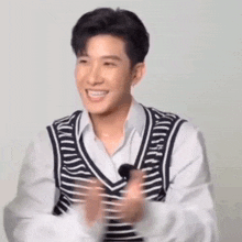 a young man wearing a striped vest and a white shirt is smiling .