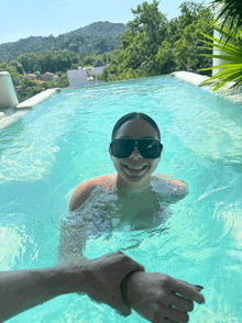 a woman wearing black sunglasses is swimming in a pool
