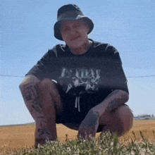 a man wearing a hat and a t-shirt is squatting down in a field .