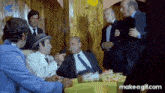 a group of men are sitting around a table and one of them is smoking a cigar