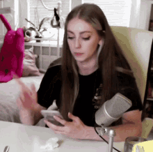 a woman sitting at a desk with a microphone looking at her cell phone