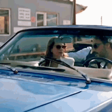 a man and a woman are sitting in a blue convertible car .