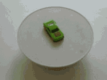 a green toy car is sitting on top of a white circle on a table .