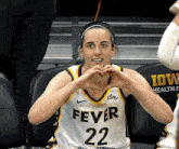 a woman wearing a fever 22 jersey makes a heart with her hands
