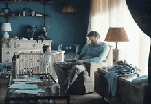 a man sits in a chair with a baby in a crib behind him