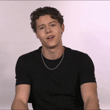 a young man with curly hair wearing a black shirt and a silver chain around his neck